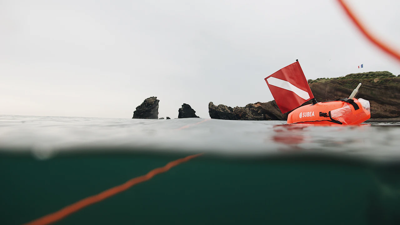 Dive flag float and line at the surface near a rocky coast