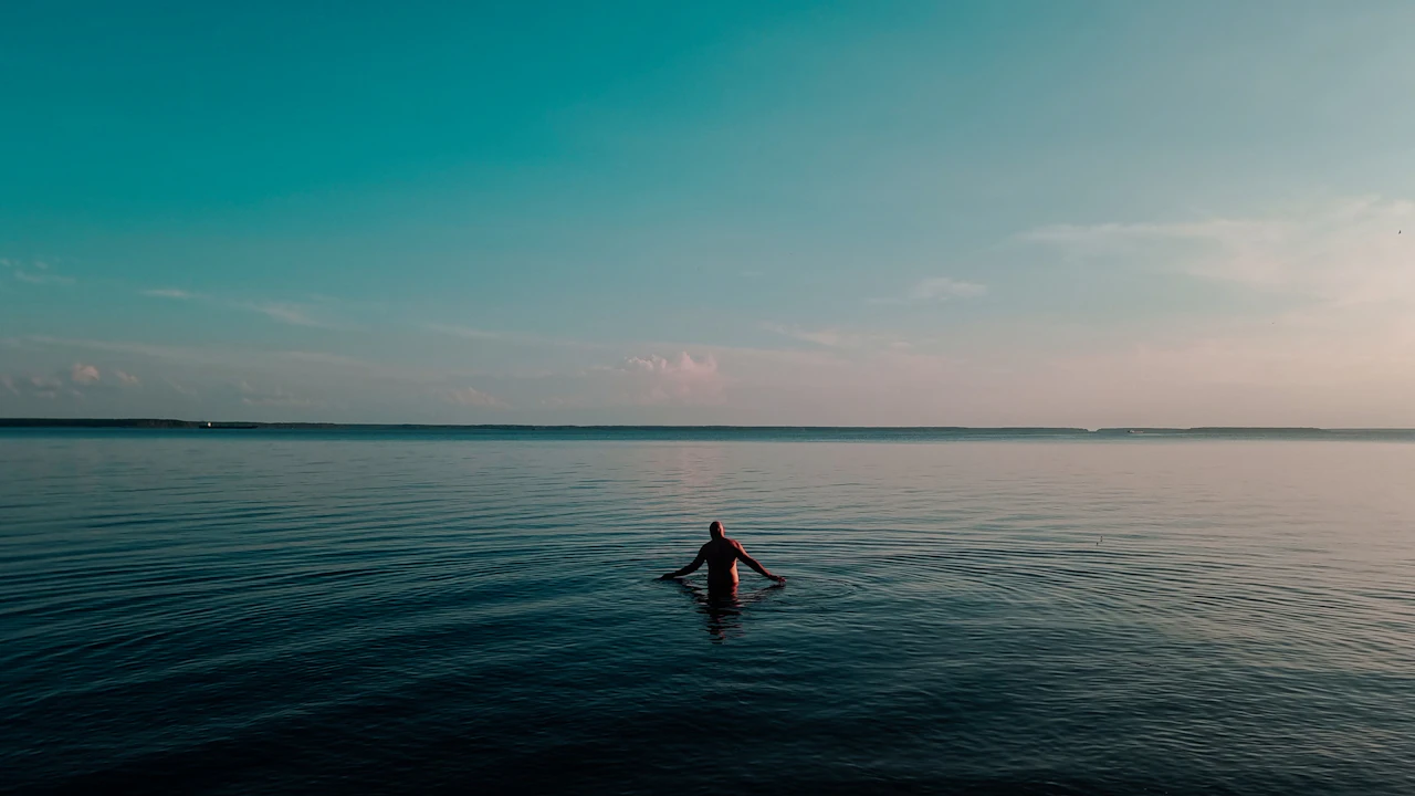 Person floating alone in a calm, still sea at dusk