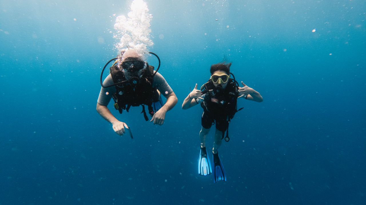 Two scuba divers descending together in clear blue water