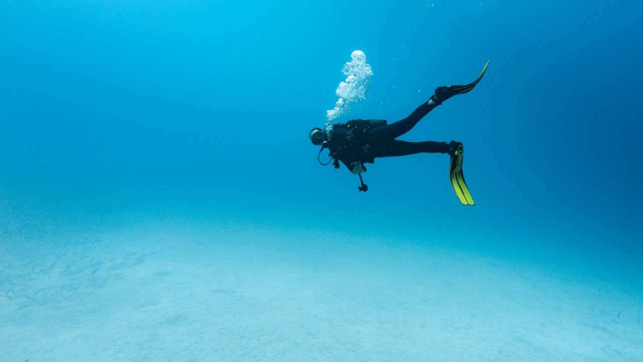 Scuba diver in yellow fins swimming above a sandy bottom in clear blue water