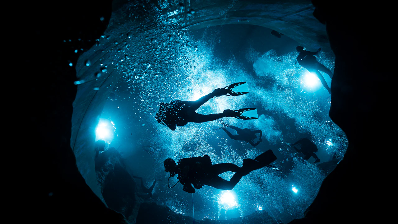 Scuba divers silhouetted against lights in a deep training pool