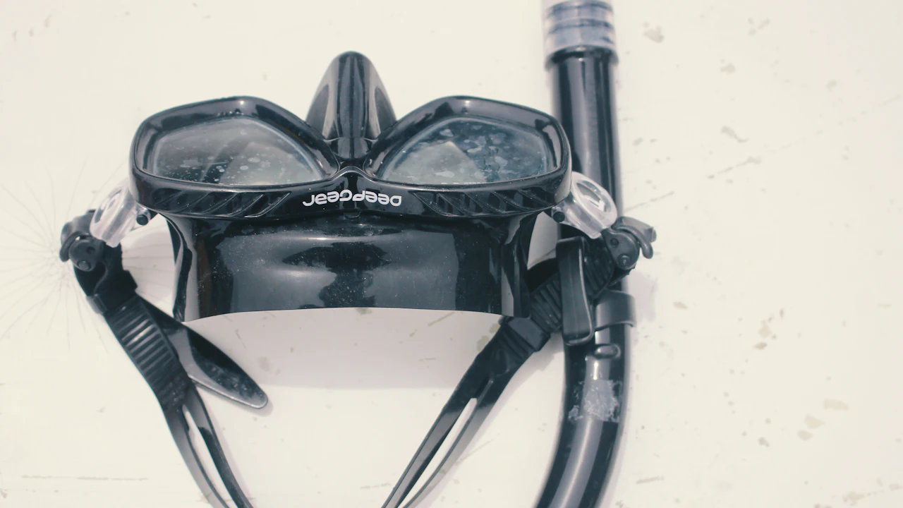 Black dive mask and snorkel on a plain surface