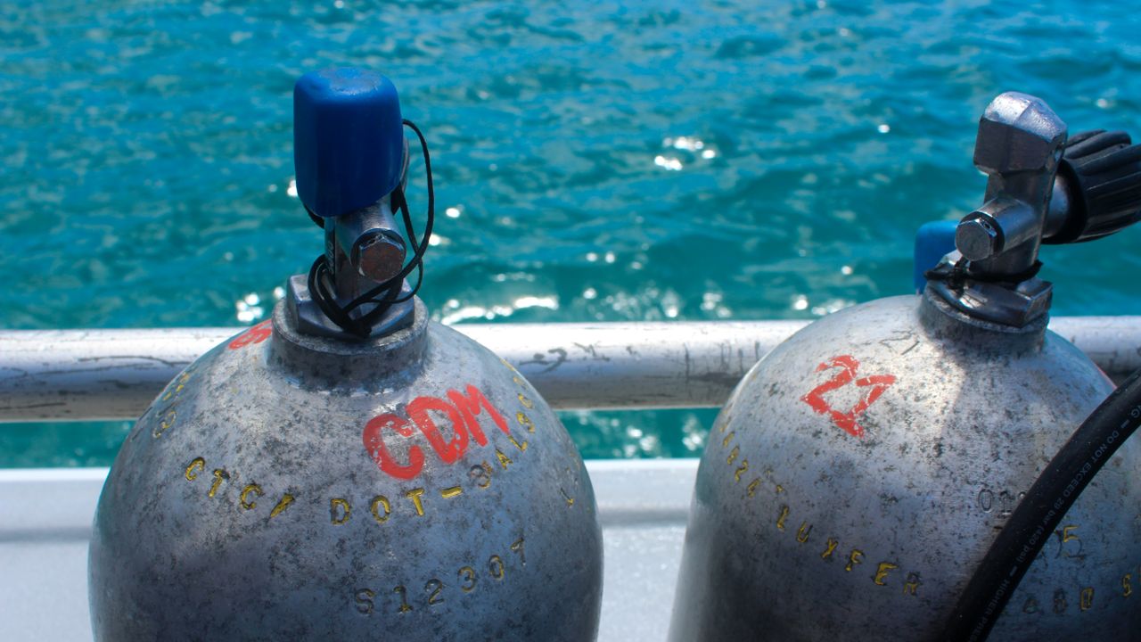 Scuba tanks with regulators attached lined up along a boat bench