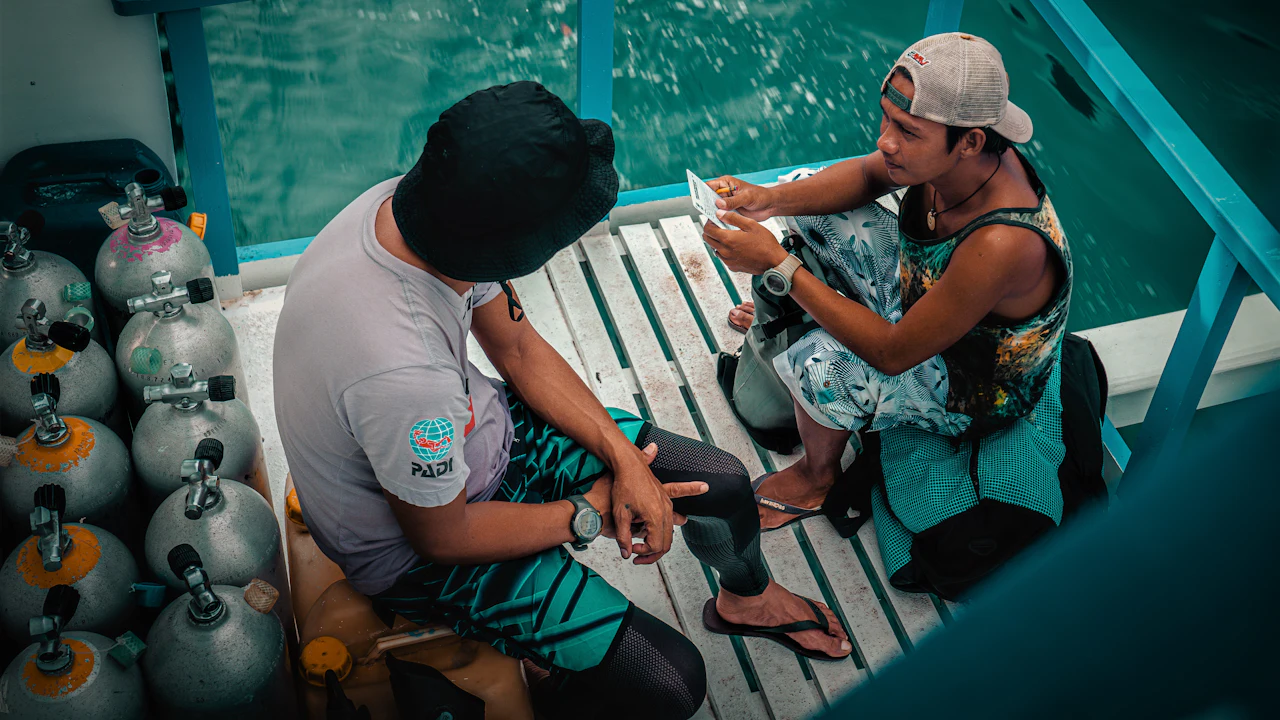 Two divers sitting on a boat bench beside scuba tanks