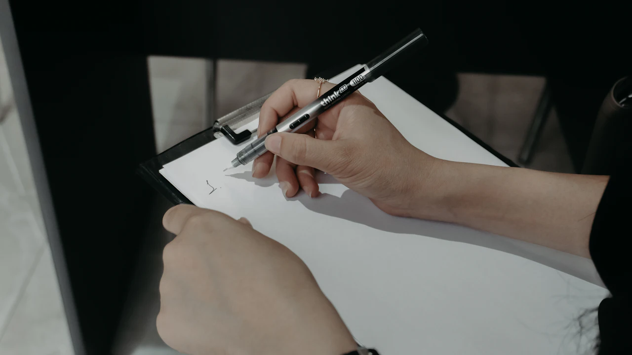 Person filling in a paper health questionnaire on a clipboard at a table