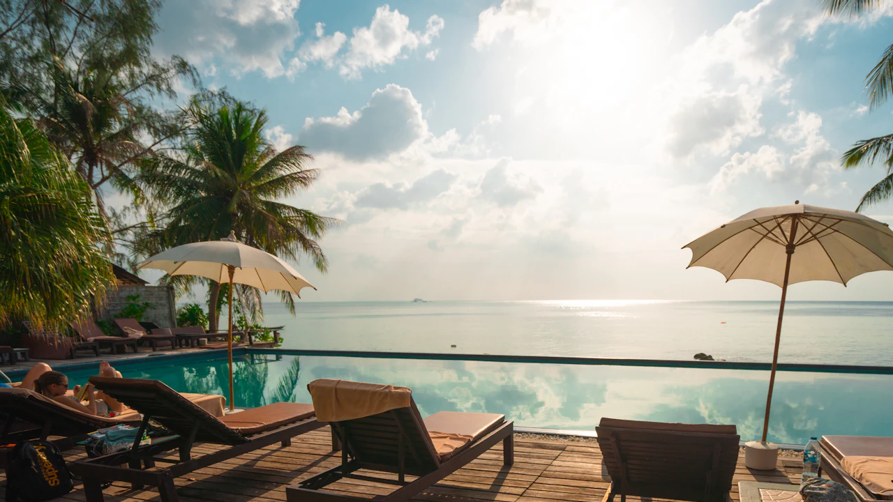 Hotel swimming pool beside a sandy beach lined with palm trees