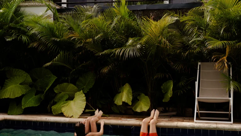 Swimmer relaxing at the edge of a resort pool among tropical plants