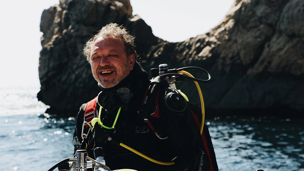 Smiling diver in scuba gear by a rocky shore