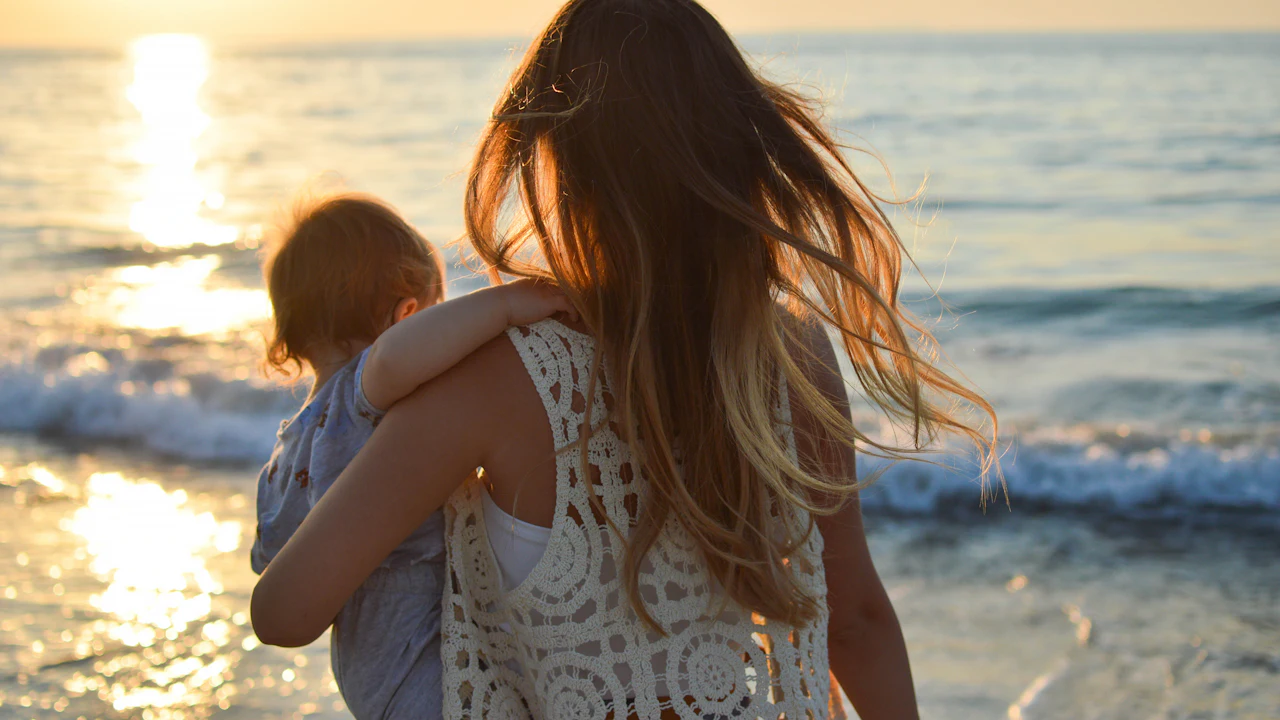 Mother holding her baby on a beach with the sea behind them