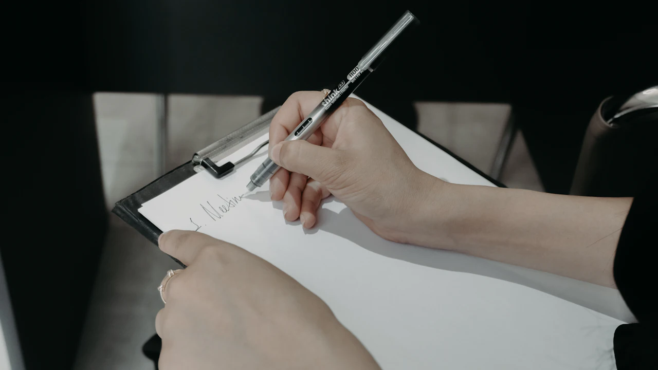 Person filling in a paper health form on a clipboard at a table