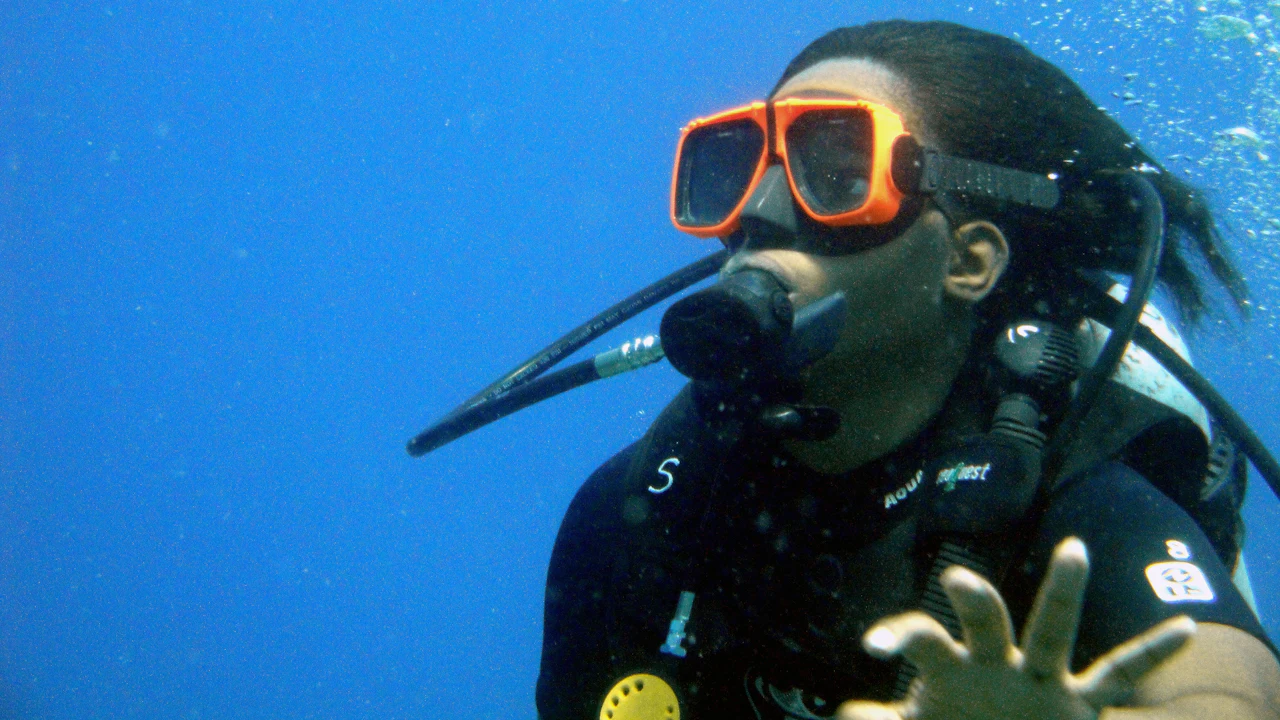 Diver in an orange mask holding up an open hand underwater