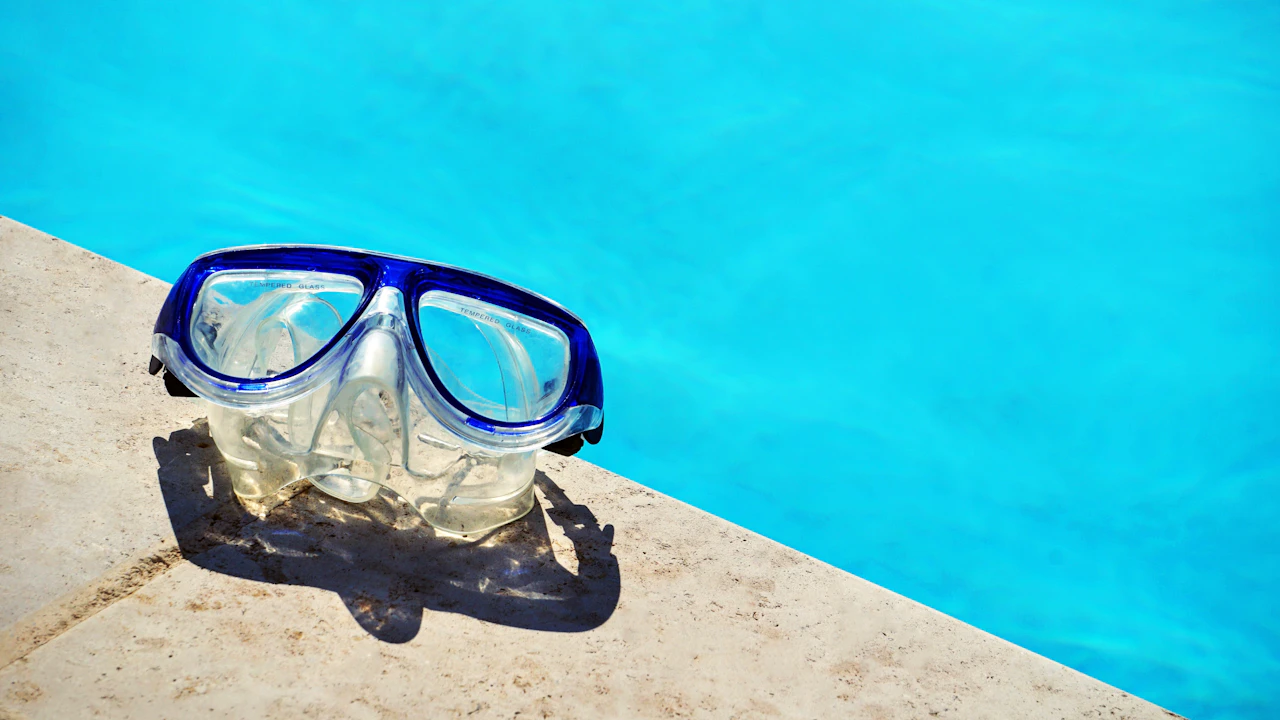 Dive mask resting on the edge of a bright blue swimming pool