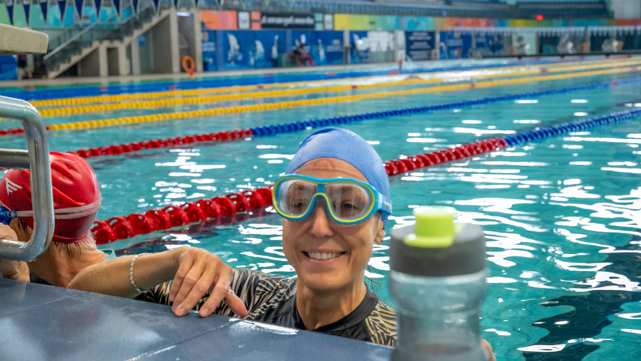 Smiling older swimmer in goggles and cap at the edge of a pool