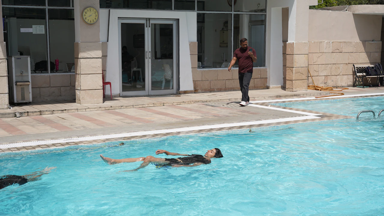 Swimmer floating on their back in an outdoor pool while a coach watches