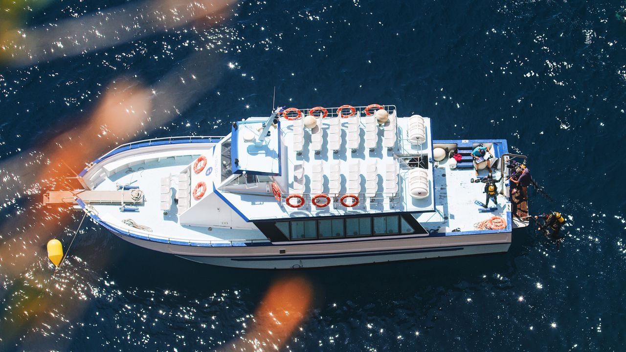 Dive boat seen from above with divers entering the water at the stern
