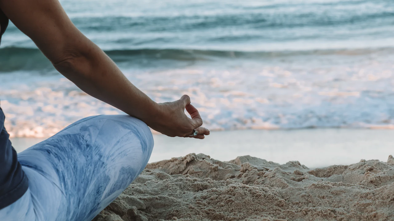 Person sitting cross-legged on a beach in a calm pose