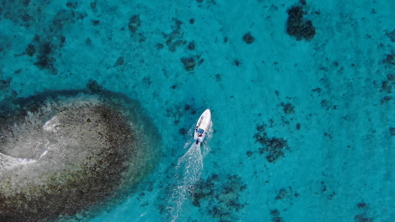 Aerial view of a small boat speeding past a sandbar and coral patches