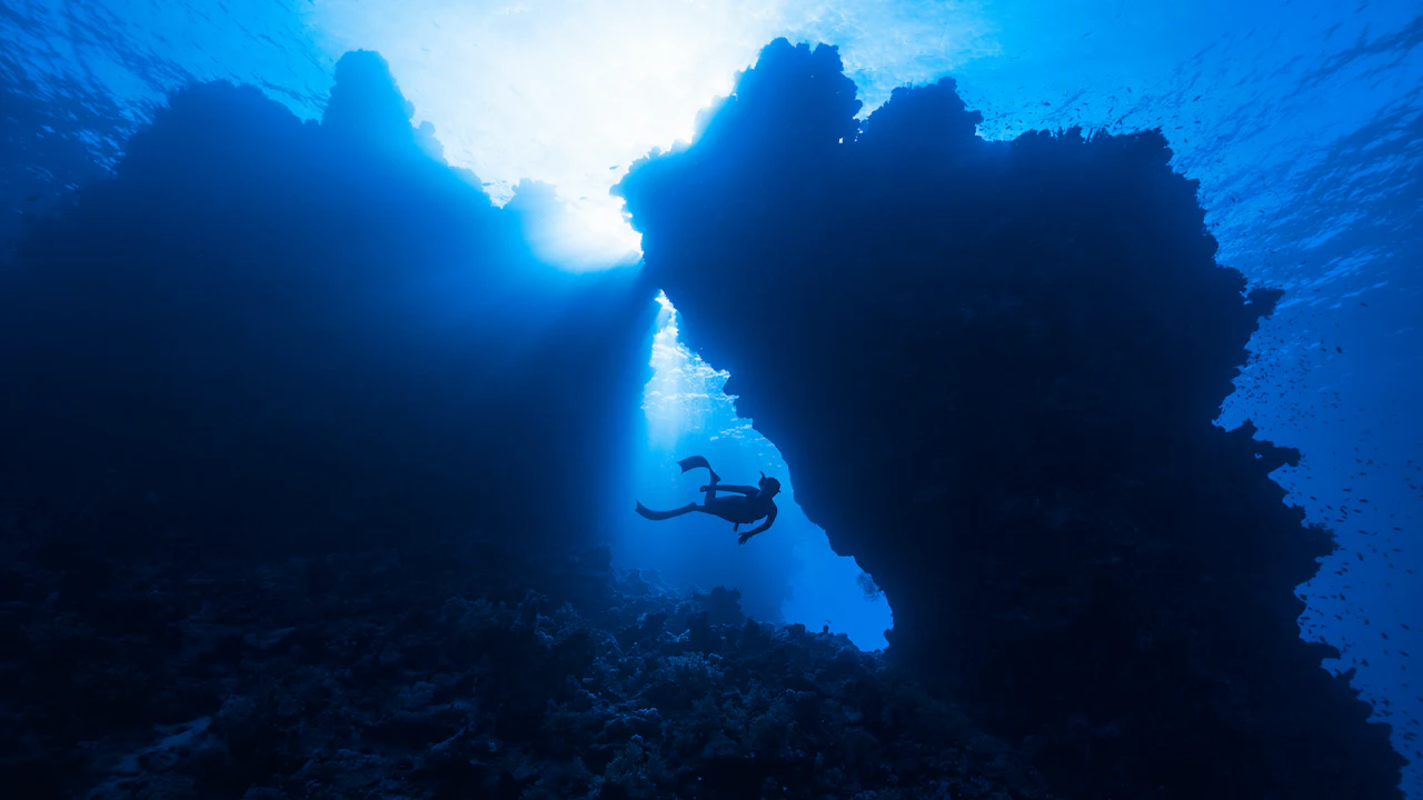 Scuba diver swimming through a reef arch in blue water