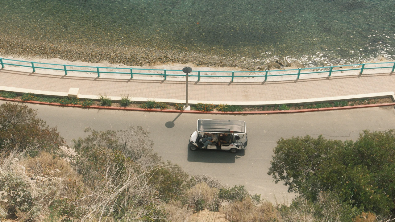 Golf cart driving along a seaside road seen from above