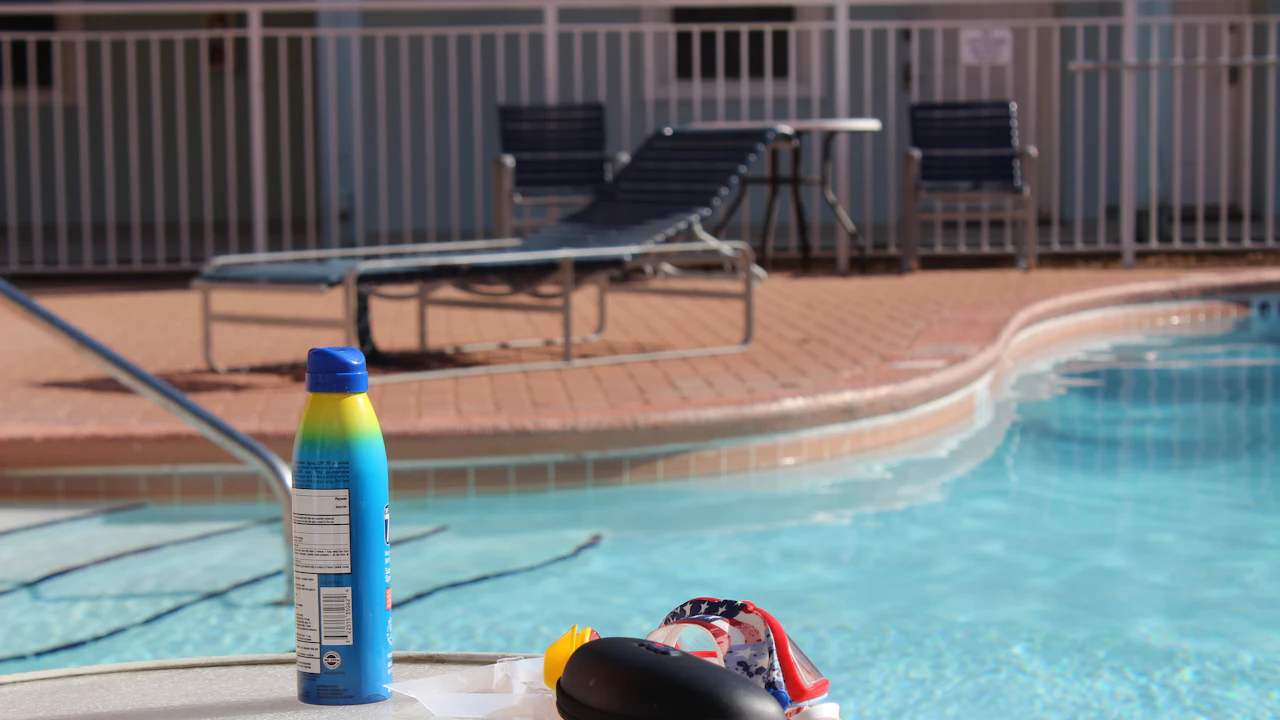 Sunscreen bottle and swim gear on the edge of a swimming pool